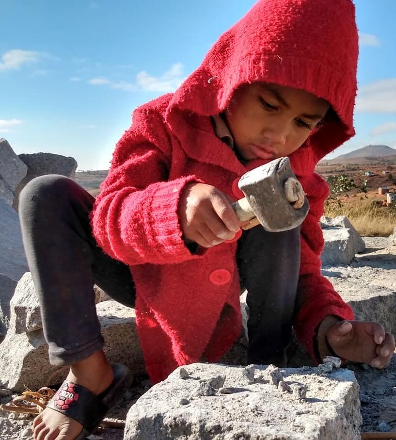 Malagasy child wearing a red hood breaking rocks